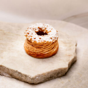 Pâtisserie ronde en pâte choux, crème pralinée, anneau croustillant et sucre glace sur pierre.