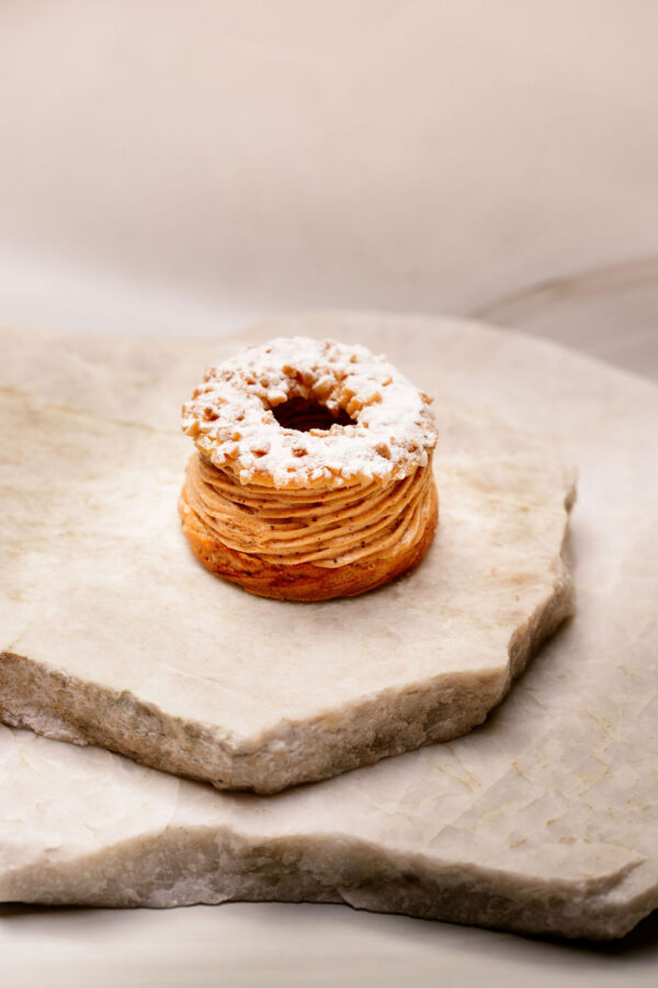 Pâtisserie ronde en pâte choux, crème pralinée, anneau croustillant et sucre glace sur pierre.