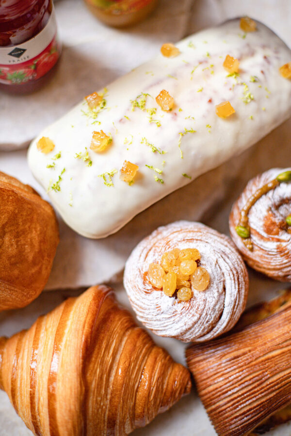 Assortiment de pâtisseries comprenant croissant, brioche aux raisins, gâteau glacé aux agrumes et viennoiserie striée.