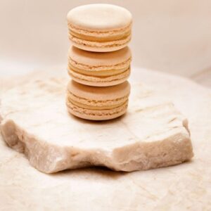 Trois macarons beiges empilés sur une plaque de marbre clair avec fond neutre.