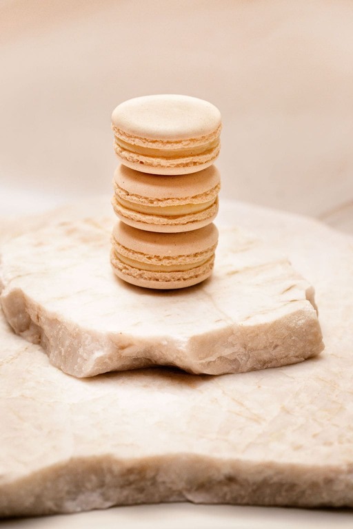 Trois macarons beiges empilés sur une plaque de marbre clair avec fond neutre.