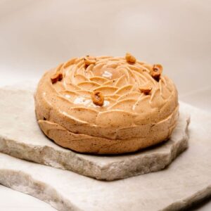 Gâteau rond glacé beige décoré de noix, posé sur deux plaques de pierre empilées.
