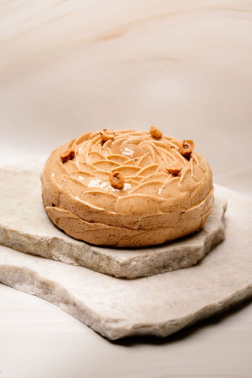 Gâteau rond glacé beige décoré de noix, posé sur deux plaques de pierre empilées.