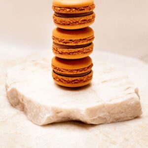 Trois macarons marron empilés sur une pierre blanche rugueuse.