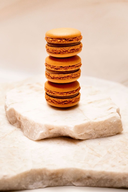 Trois macarons marron empilés sur une pierre blanche rugueuse.