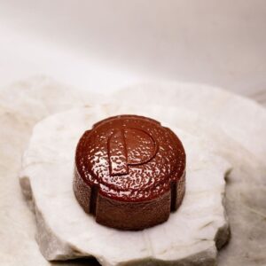 Savon rond marron avec la lettre P gravée posé sur deux plaques de pierre blanche.