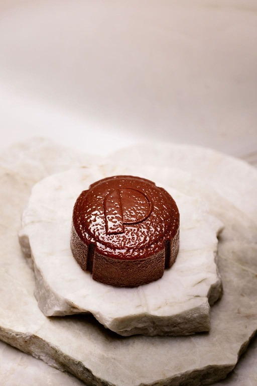 Savon rond marron avec la lettre P gravée posé sur deux plaques de pierre blanche.