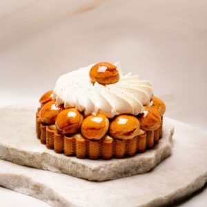 Tartelette aux choux glacés caramel et crème fouettée en spirale sur pierre blanche.