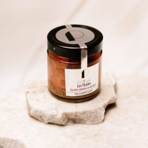 Pot en verre de pickles de carottes aux agrumes avec couvercle noir sur pierre claire.