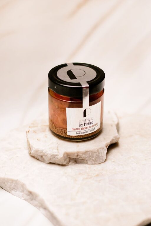 Pot en verre de pickles de carottes aux agrumes avec couvercle noir sur pierre claire.