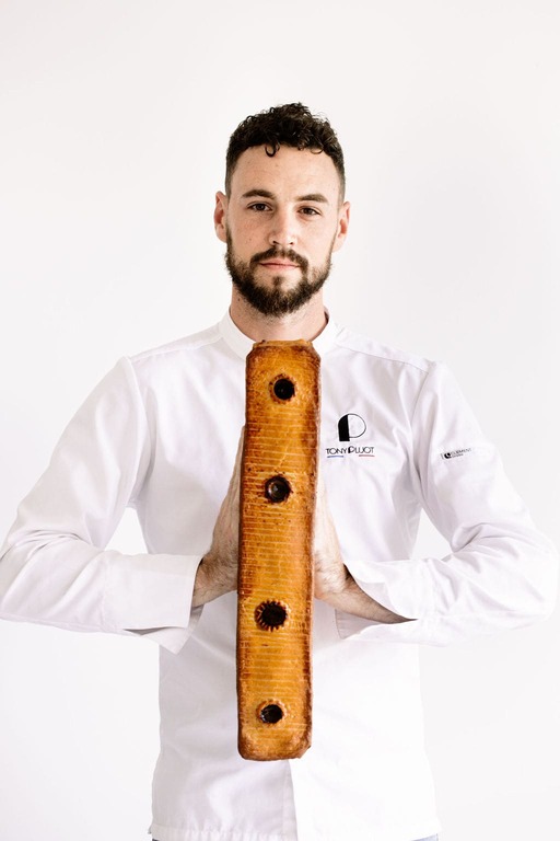 Homme en veste de chef tenant verticalement un pâté rectangulaire avec quatre ouvertures.