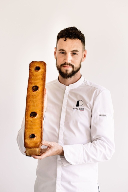 Homme en veste de chef blanc tenant un pâté en croûte rectangulaire avec quatre ouvertures.