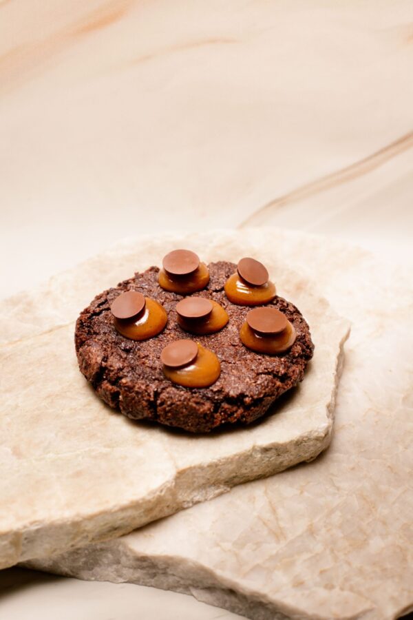 Cookie au chocolat avec six boules de caramel et disques de chocolat sur plaque de pierre.