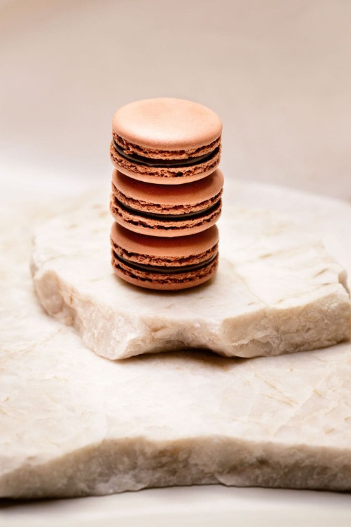 Trois macarons au chocolat empilés sur deux plaques de marbre clair.
