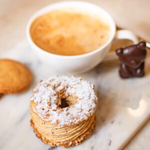 Tasse de café avec mousse, pâtisserie en anneau saupoudrée de sucre glace, biscuit et chocolat en forme d'ourson sur marbre.