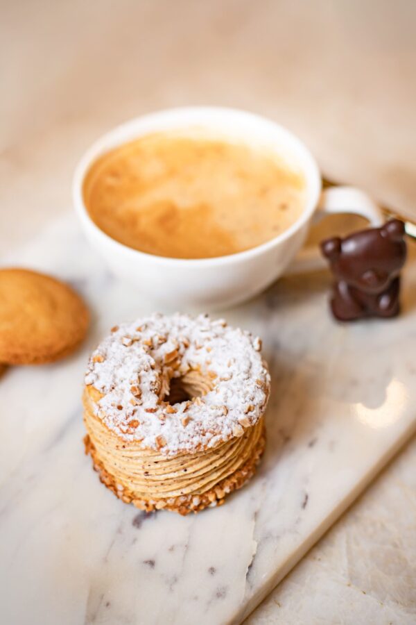 Tasse de café avec mousse, pâtisserie en anneau saupoudrée de sucre glace, biscuit et chocolat en forme d'ourson sur marbre.