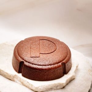 Objet circulaire en métal cuivré gravé d'un P posé sur deux plaques de pierre blanche.