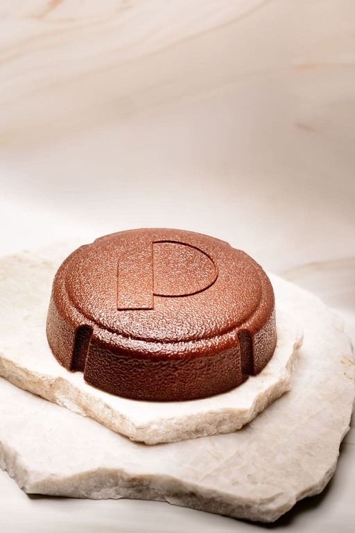 Objet circulaire en métal cuivré gravé d'un P posé sur deux plaques de pierre blanche.