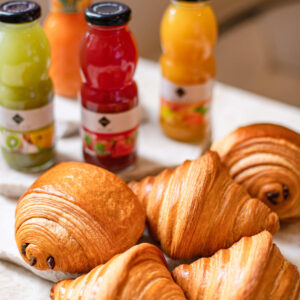 Cinq viennoiseries variées posées devant quatre bouteilles de jus de fruits colorés.