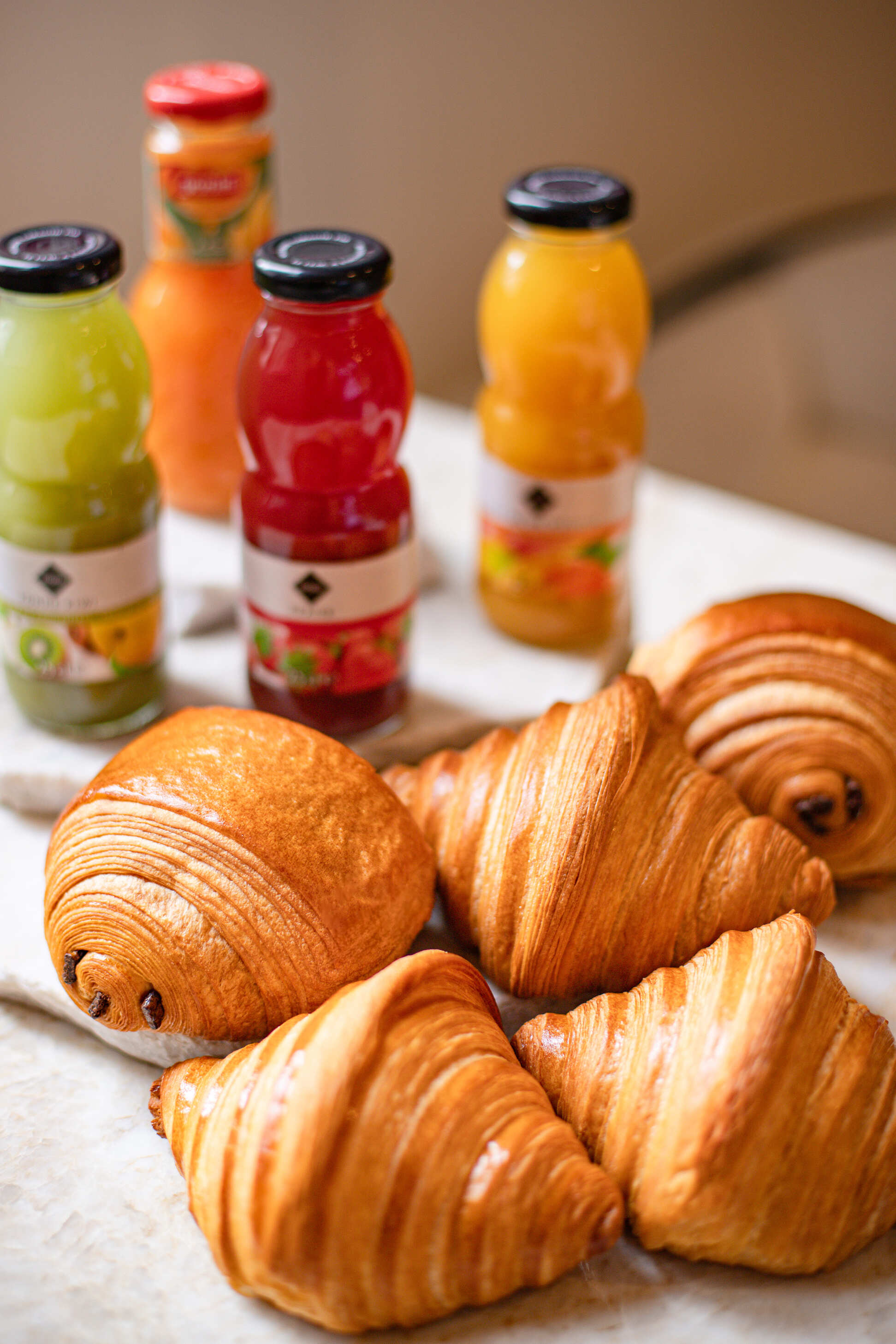 Cinq viennoiseries variées posées devant quatre bouteilles de jus de fruits colorés.