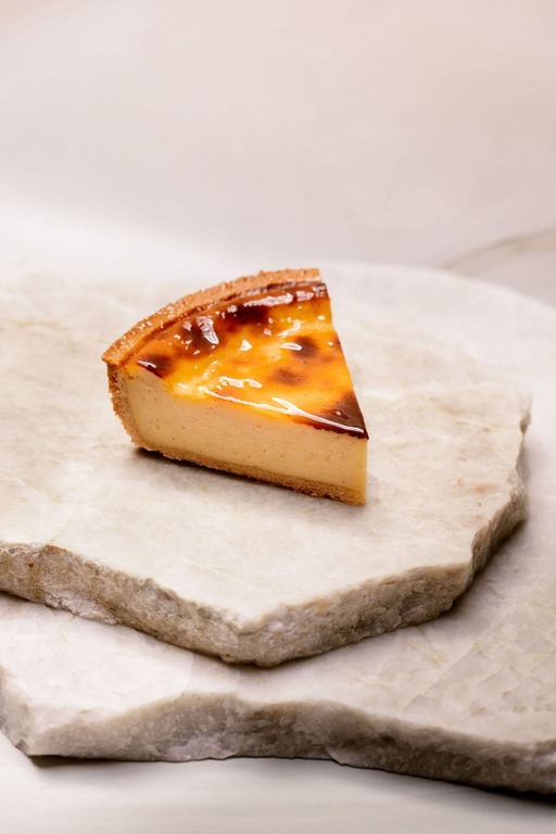 Part de flan pâtissier posée sur deux plaques de marbre blanc superposées.