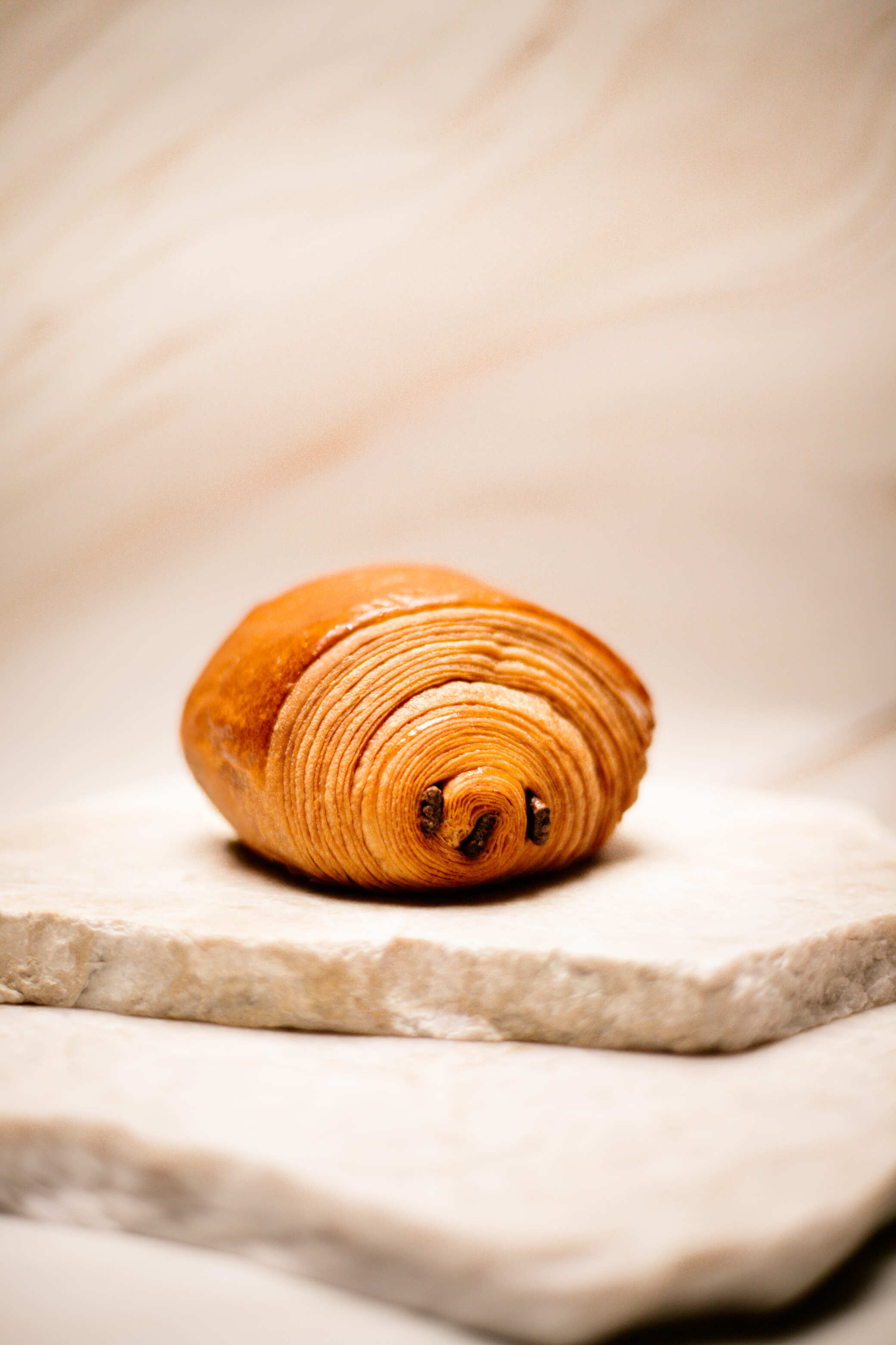 Pain au chocolat frais sur une plaque en pierre beige claire.
