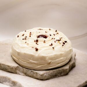 Gâteau rond sans gluten décoré de crème chantilly et éclats de cacao sur plaques de pierre.