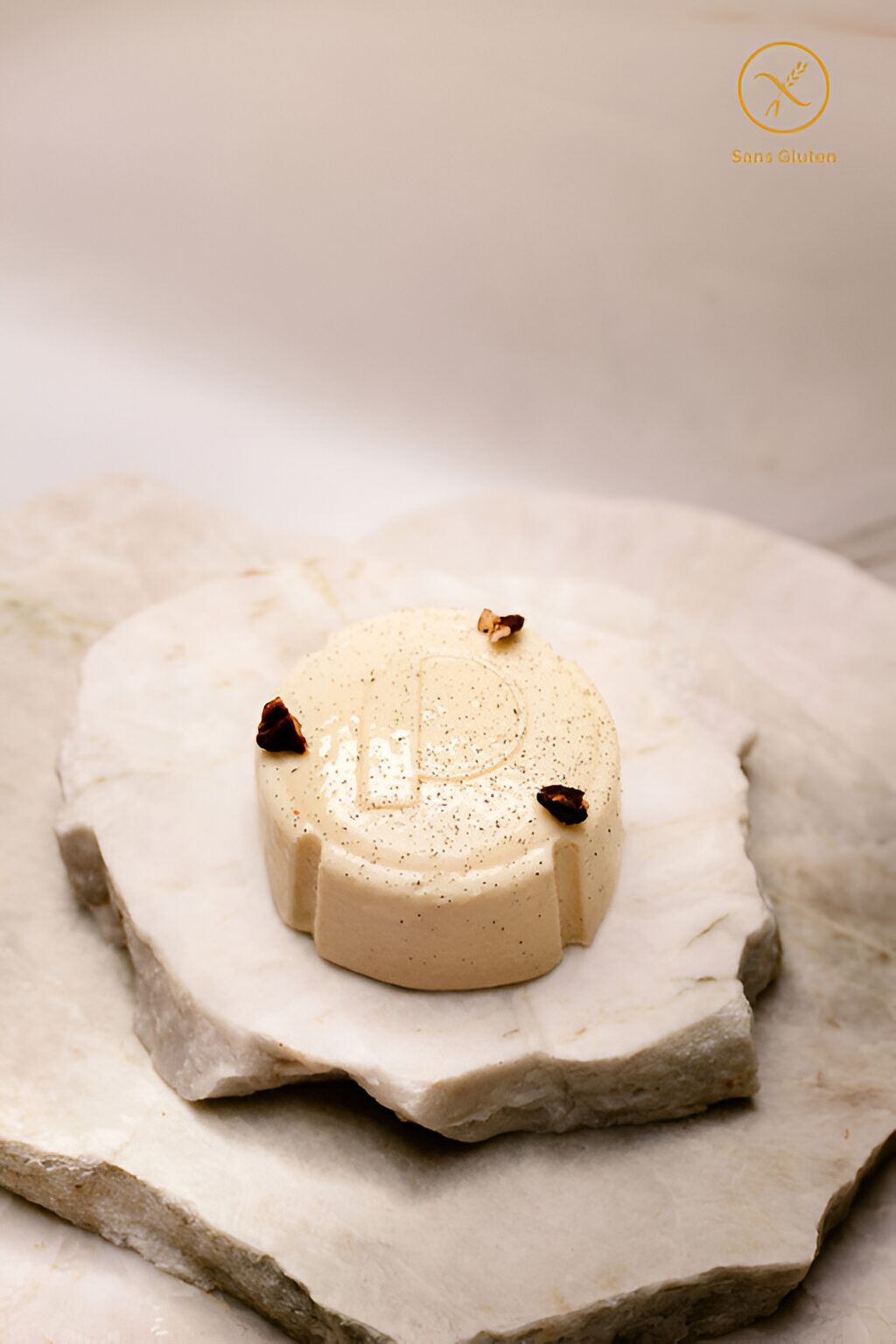 Petit dessert beige clair rond avec décor brun posé sur pierre blanche, label sans gluten.