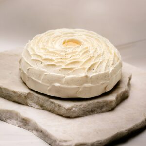 Gâteau rond sans gluten glacé de crème blanche en spirale, posé sur plaques de pierre.