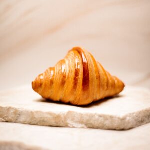 Croissant doré posé sur deux plaques de pierre beige avec fond flou.