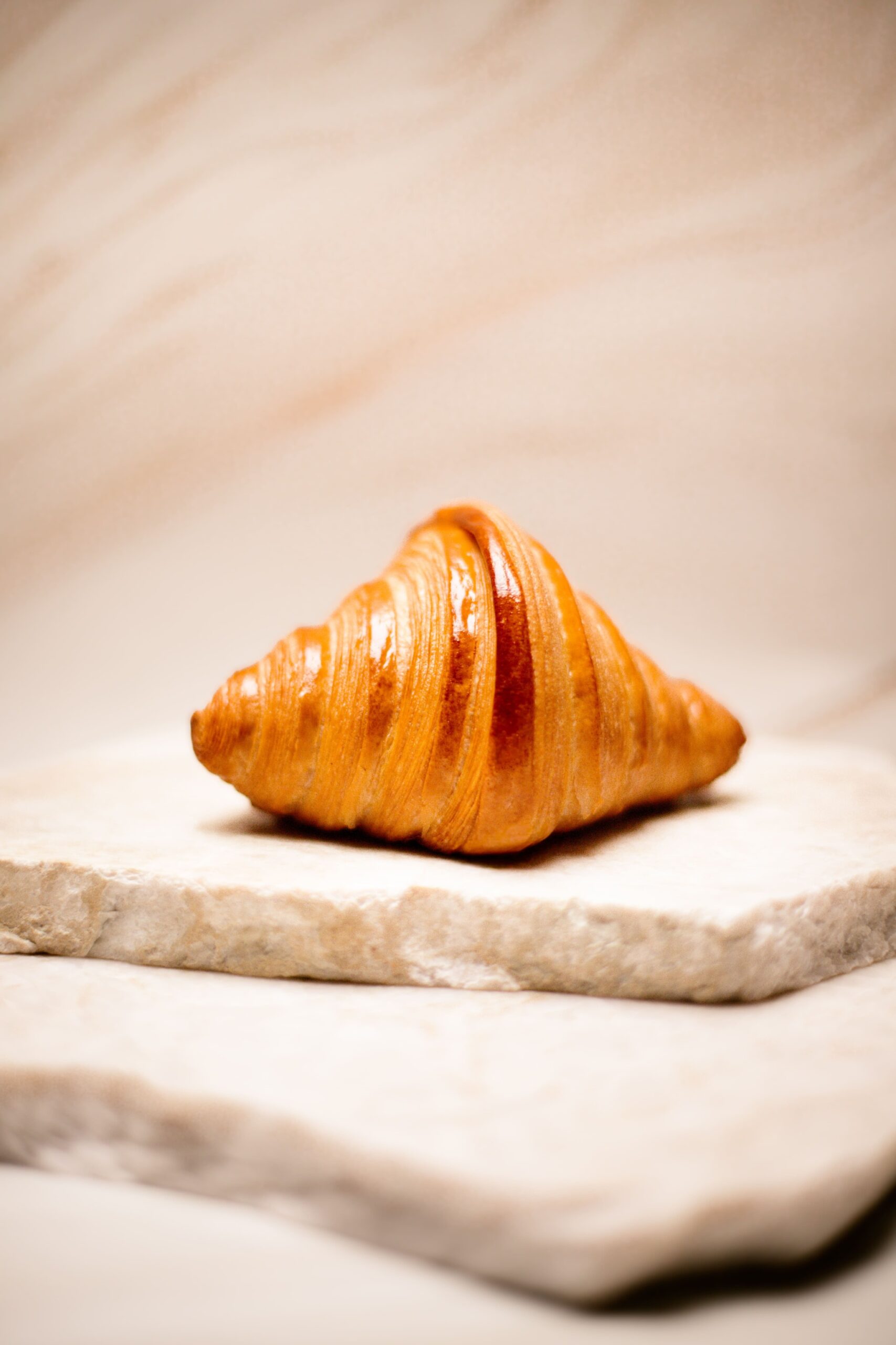 Croissant doré posé sur deux plaques de pierre beige avec fond flou.