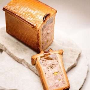 Terrine pâtissière dorée rectangulaire avec farce viande hachée et pistaches tranchée sur pierre blanche.