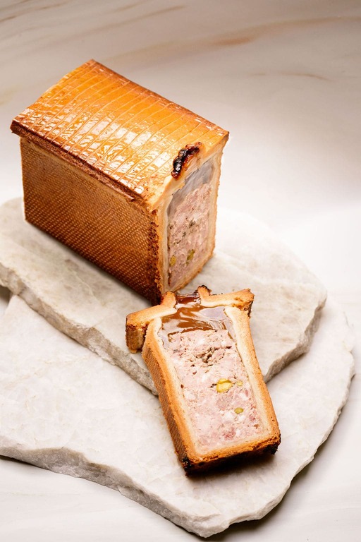 Terrine pâtissière dorée rectangulaire avec farce viande hachée et pistaches tranchée sur pierre blanche.
