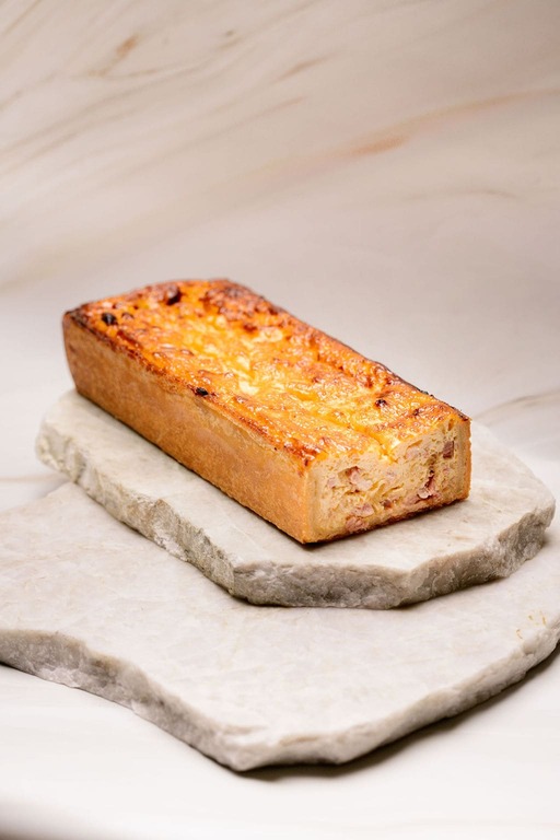 Quiche rectangulaire dorée posée sur deux pierres plates empilées.