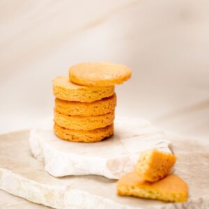 Pile de biscuits ronds dorés sur pierre blanche avec un biscuit cassé à côté, fond flou.