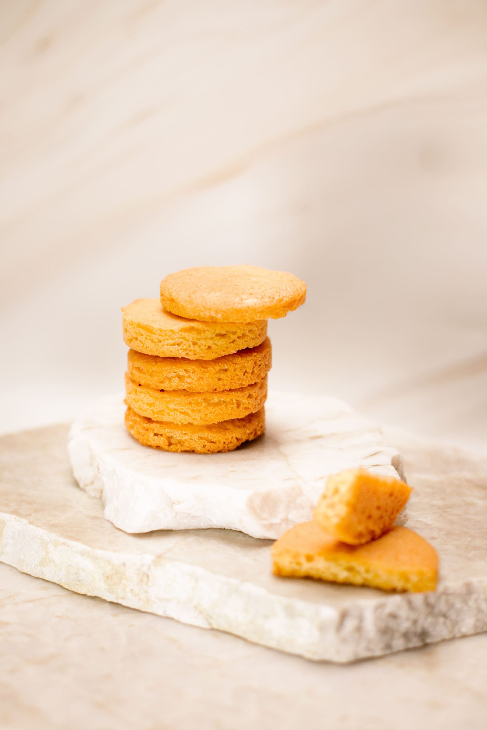 Pile de biscuits ronds dorés sur pierre blanche avec un biscuit cassé à côté, fond flou.