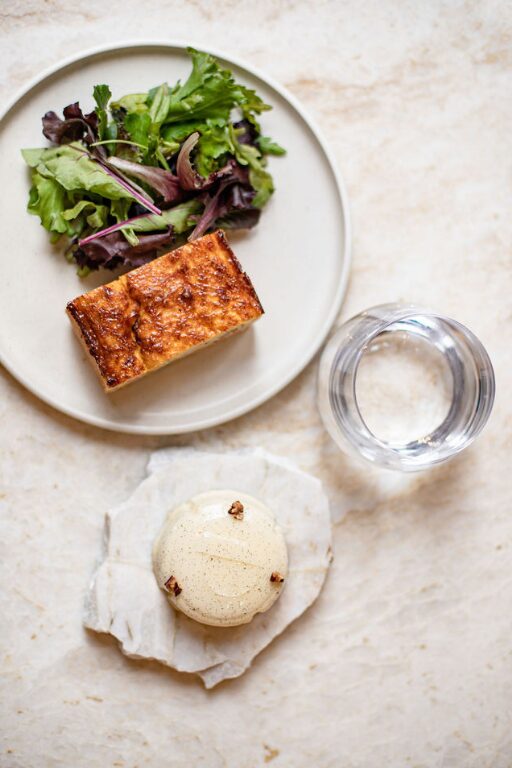Assiette avec quiche, salade verte, verre d'eau et dessert crème sur pierre plate.