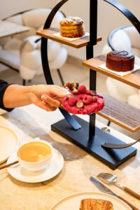 Main saisissant un biscuit framboise sur un présentoir à pâtisseries avec une tasse de café.