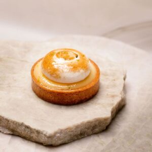 Tartelette au citron avec meringue dorée servie sur deux pierres plates claires.
