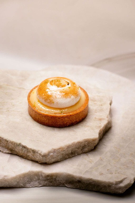 Tartelette au citron avec meringue dorée servie sur deux pierres plates claires.