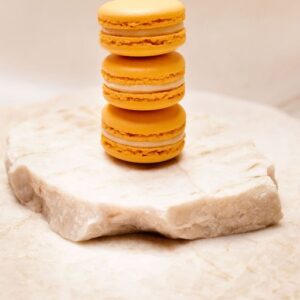 Trois macarons orange empilés sur un bloc de marbre blanc texturé.