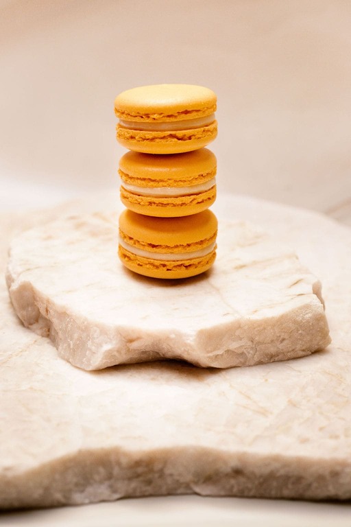 Trois macarons orange empilés sur un bloc de marbre blanc texturé.