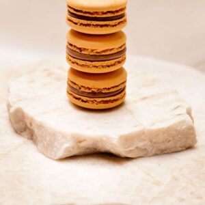 Trois macarons orange empilés sur une plaque de pierre blanche.