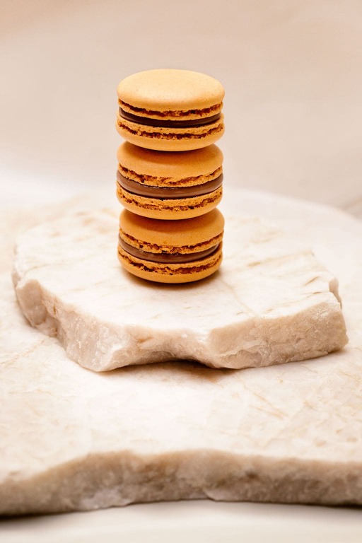 Trois macarons orange empilés sur une plaque de pierre blanche.