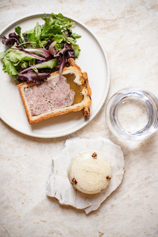 Assiette avec pâté en croûte, salade verte, verre d'eau et dessert sur pierre.