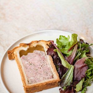 Tranche de pâté en croûte avec salade de jeunes pousses sur assiette blanche.