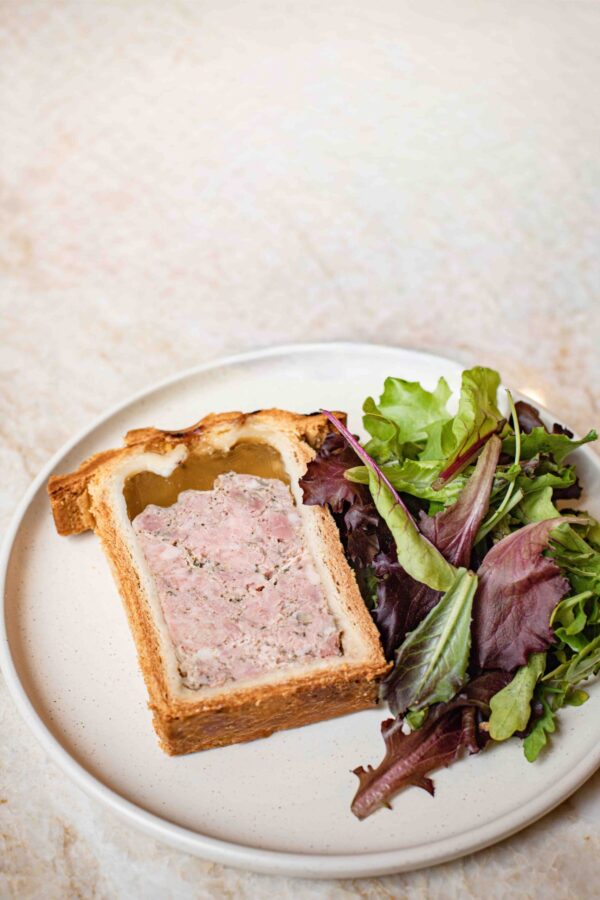 Tranche de pâté en croûte avec salade de jeunes pousses sur assiette blanche.