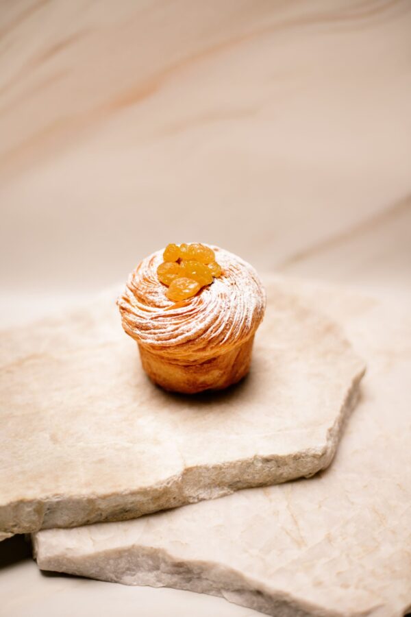 Petit gâteau feuilleté avec raisins dorés et sucre glace sur plaque de pierre beige.