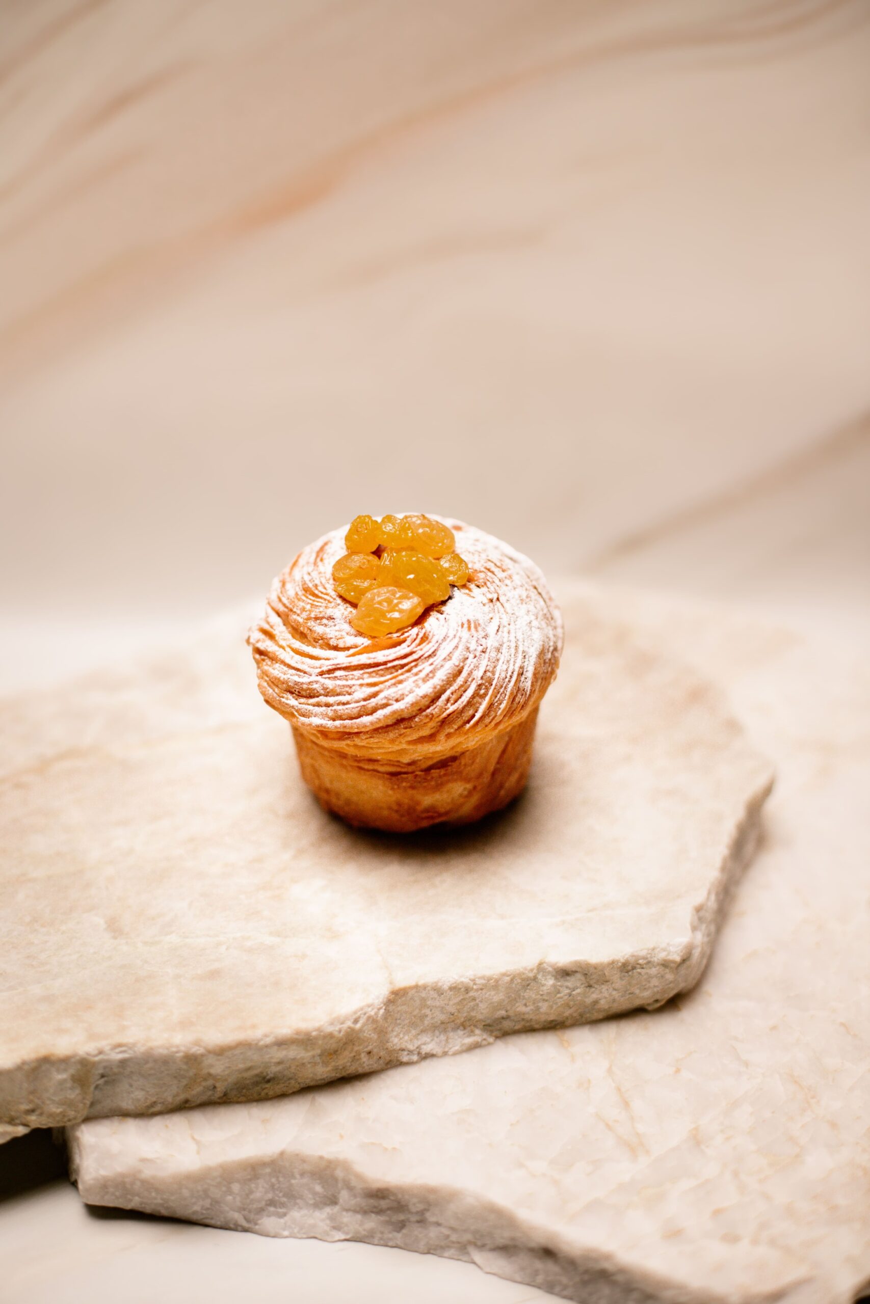 Petit gâteau feuilleté avec raisins dorés et sucre glace sur plaque de pierre beige.