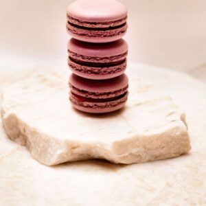 Trois macarons roses empilés sur une pierre blanche aux bords irréguliers.